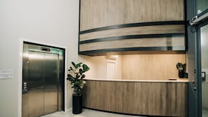 An elevator, reception desk, and a potted plant in a modern lobby. - Warners At The Bay (Warners Bay)