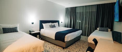 A hotel room with two beds, a nightstand, a desk, and a large window with curtains.