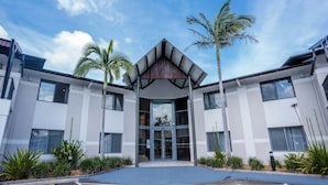 A modern building with a central entrance, surrounded by palm trees and a landscaped area. - Warners At The Bay (Warners Bay)