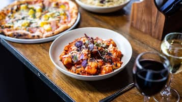 A wooden table with a pizza, a bowl of pasta, and a glass of red wine.