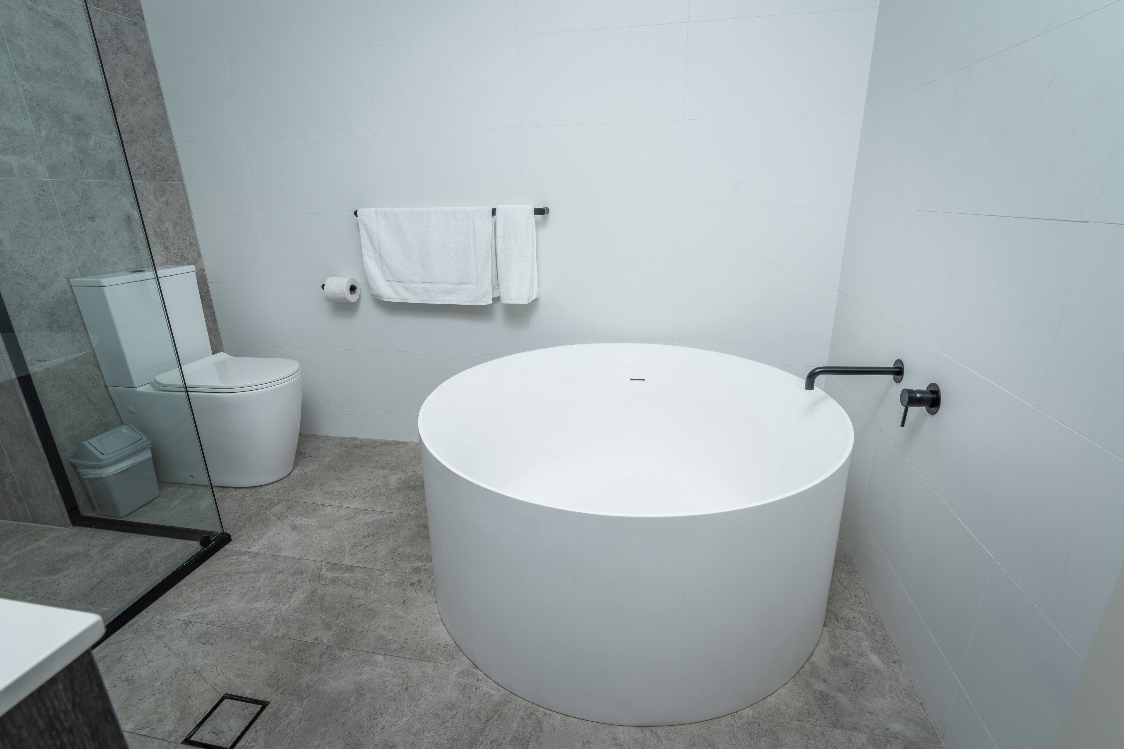 A modern bathroom with a large white bathtub, a toilet, and a glass shower enclosure.