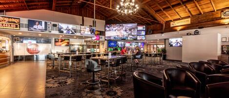 A spacious bar area with multiple screens displaying sports events, comfortable seating, and a wooden ceiling.