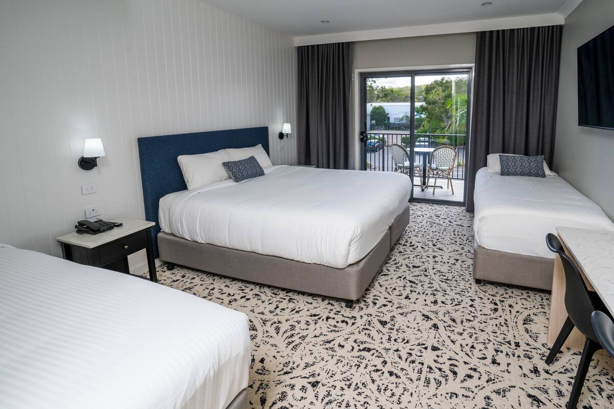A hotel room with a large bed, two bedside tables, a desk, a chair, and a balcony with outdoor seating.