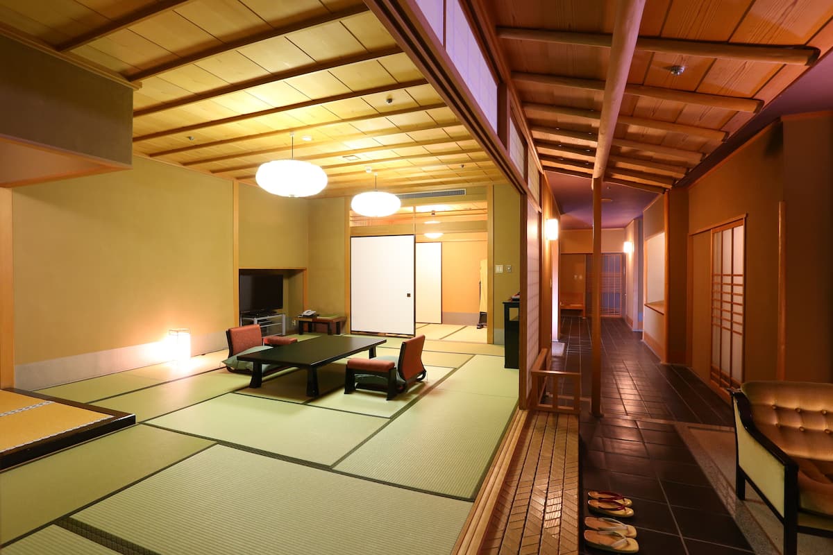 Una habitación tradicional con estera de tatami, una mesa baja y sillas, una puerta corredera y un pasillo de madera.