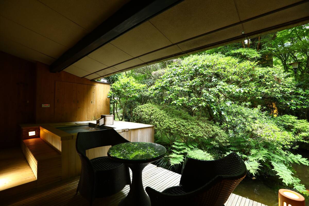 Una terraza de madera con una mesa y sillas, con vistas a un jardín exuberante y un estanque.