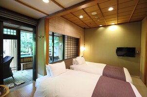 Habitación de hotel con dos camas, un televisor montado en la pared y vista a un jardín por una puerta corredera.
