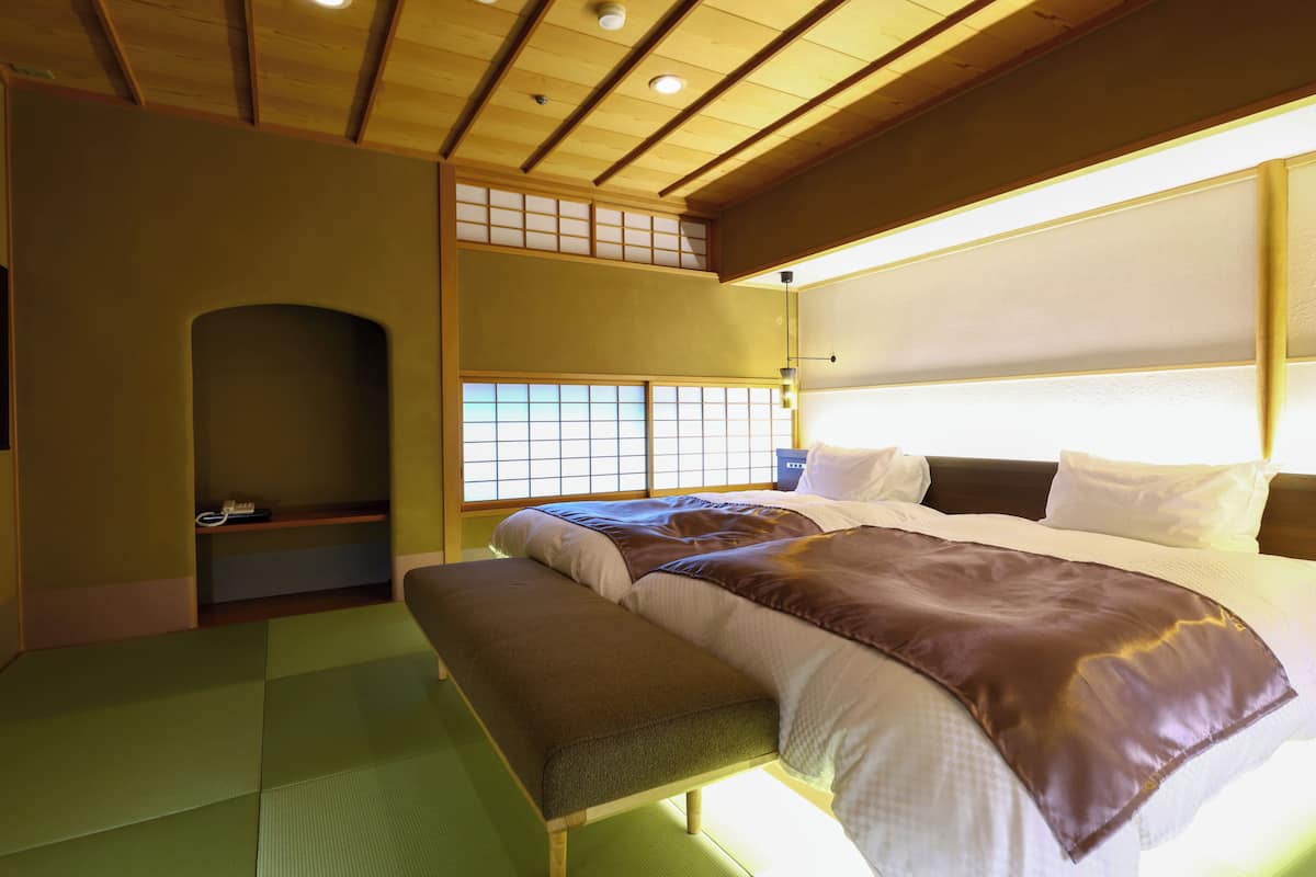 Una habitación tradicional japonesa con suelo de tatami, techo de madera bajo y una cama grande con una manta marrón.