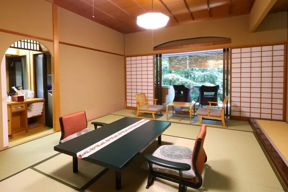 Una habitación de tatami con una mesa baja, sillas y vistas a la vegetación exterior.