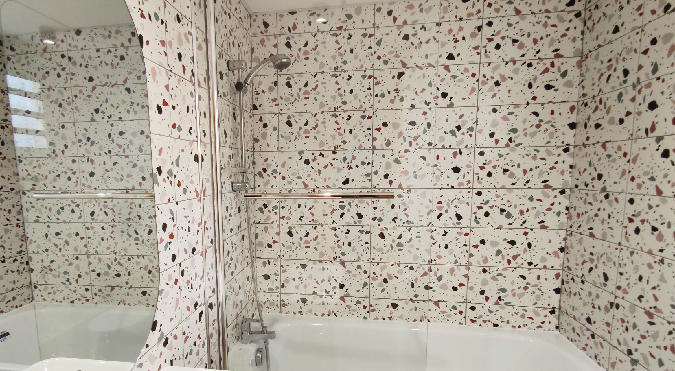 A modern bathroom with a freestanding bathtub, a glass-enclosed shower, and terrazzo tile walls.