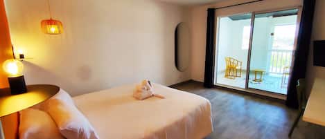 A hotel room with a bed, a lamp, a mirror, and a view of the outside balcony.