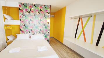 A hotel room with a bed, a small seating area, a wall with a geometric pattern, and a window with colorful curtains.