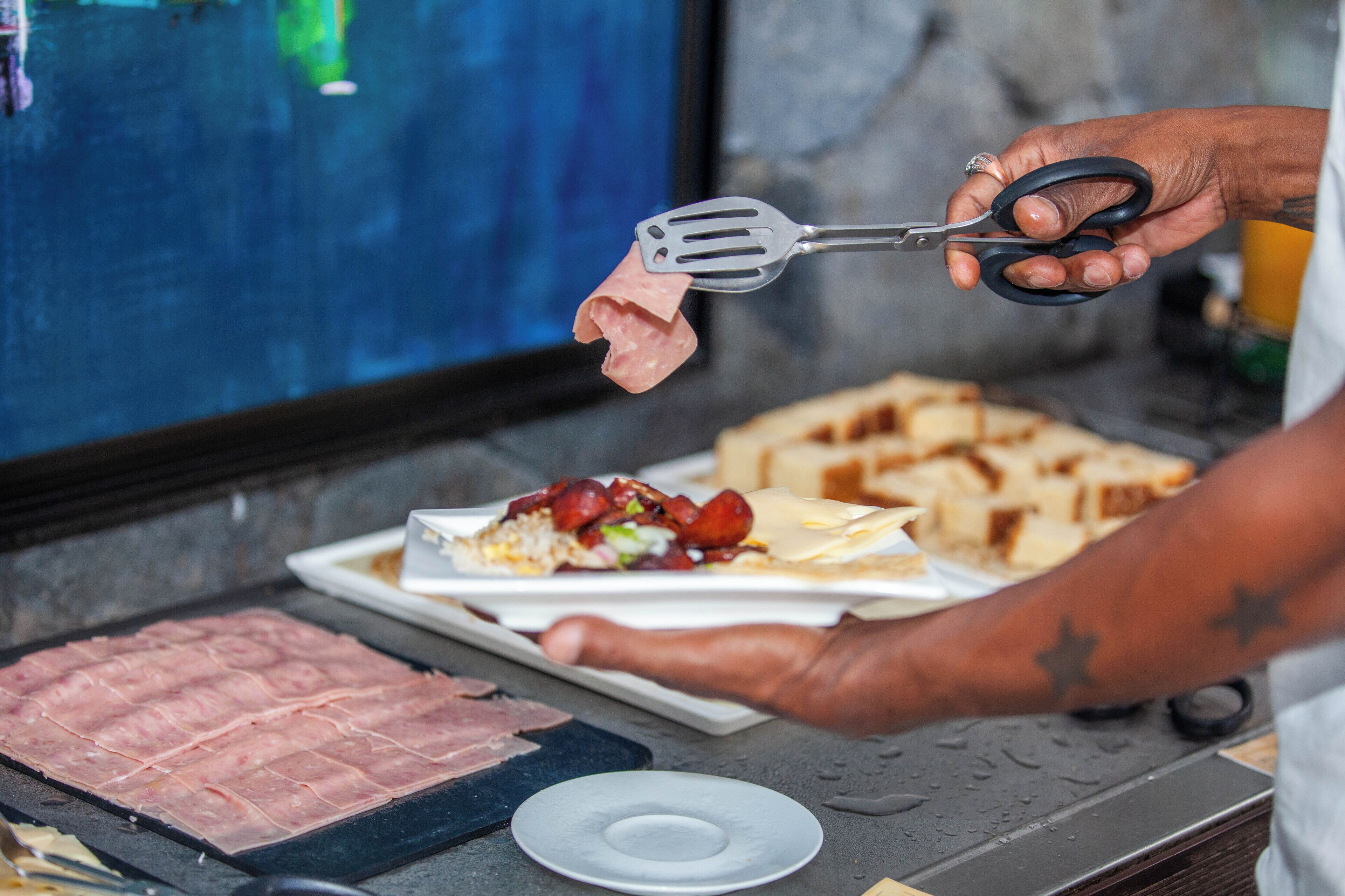 Une personne prépare des aliments sur un gril, avec une assiette de viande tranchée et une spatule à proximité.