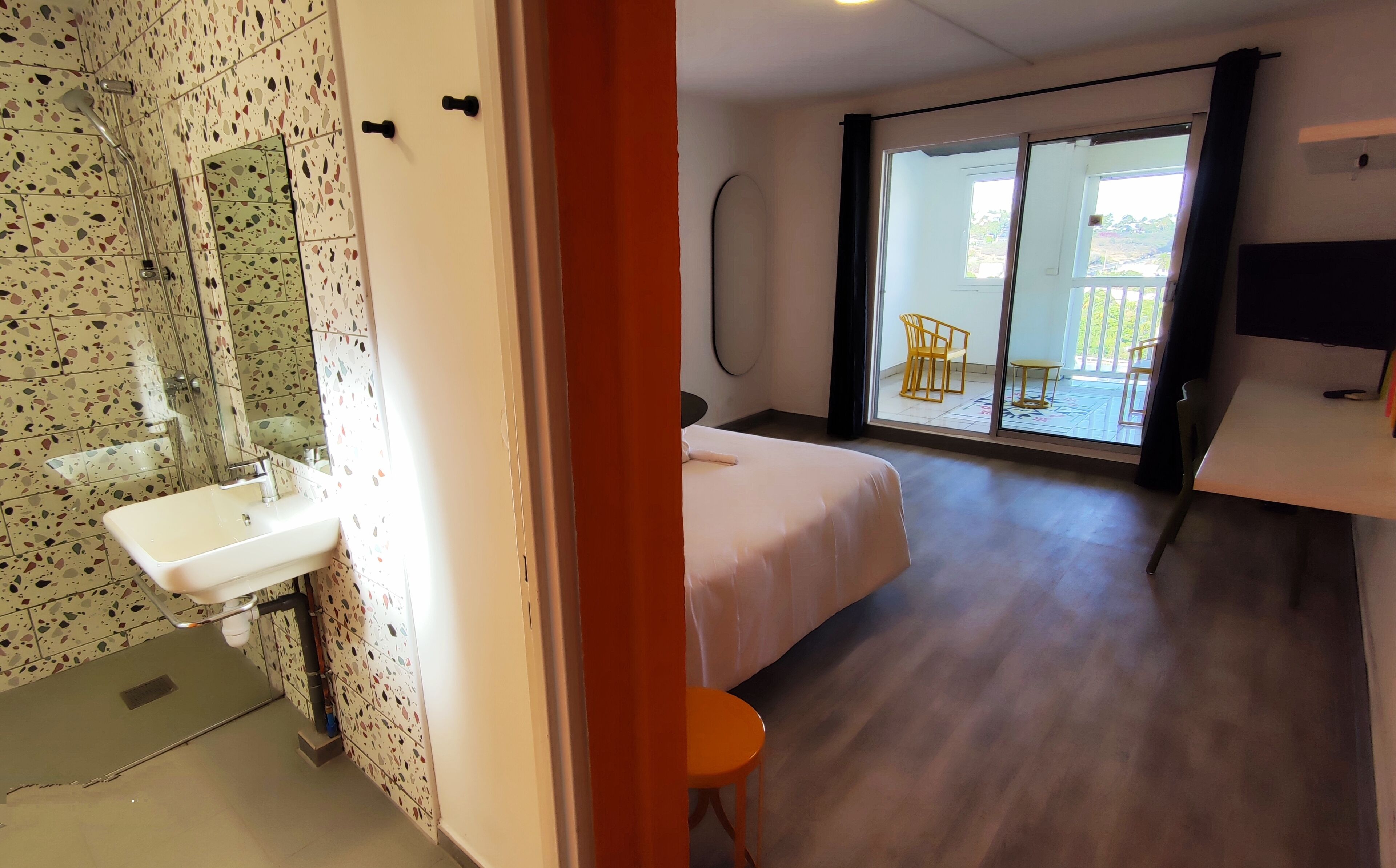 Habitación de hotel con baño, una cama, una mesita pequeña y un balcón con sillas.