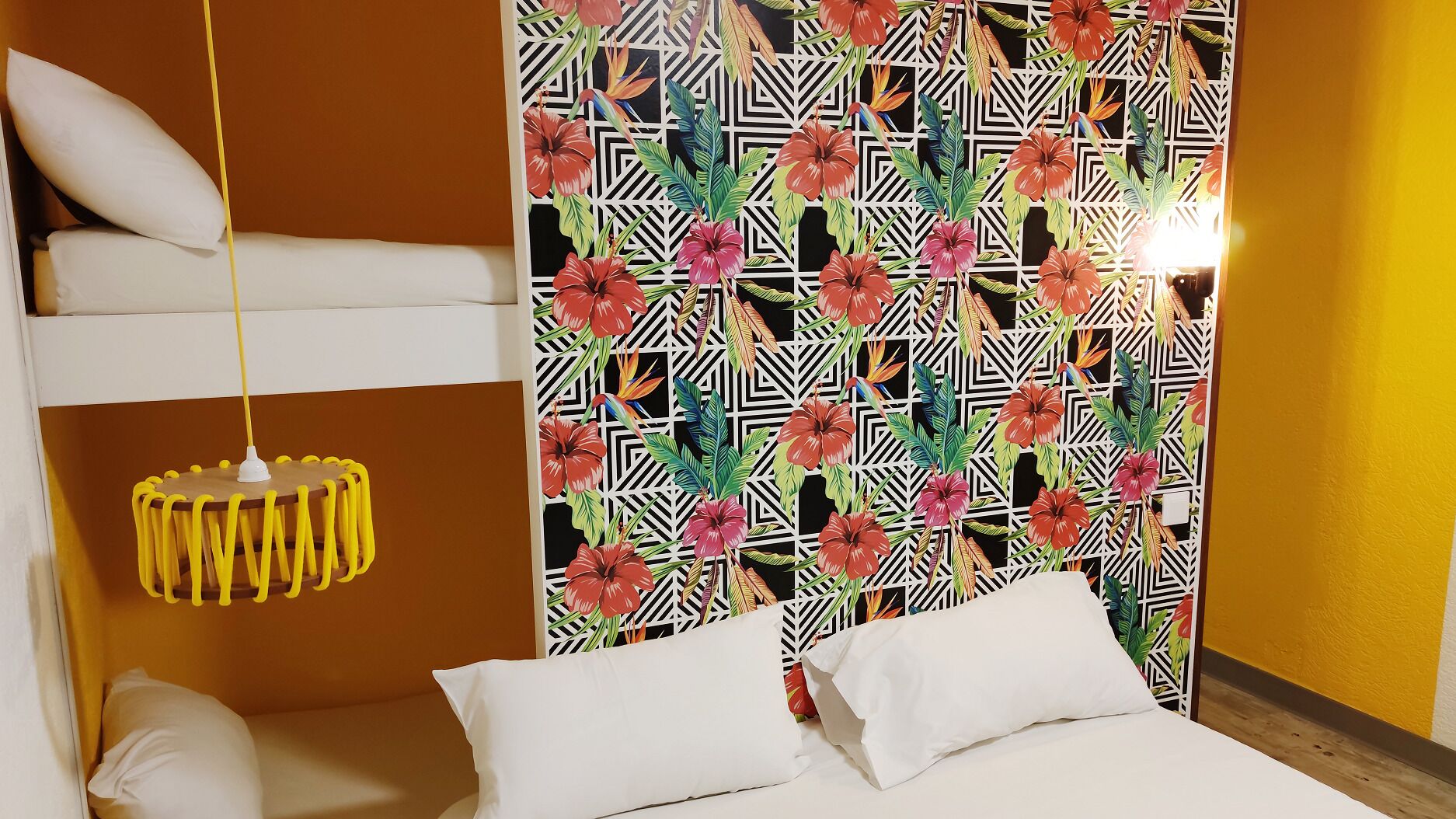 A bedroom with a bunk bed, a hanging yellow lamp, and a wall with a tropical floral pattern.