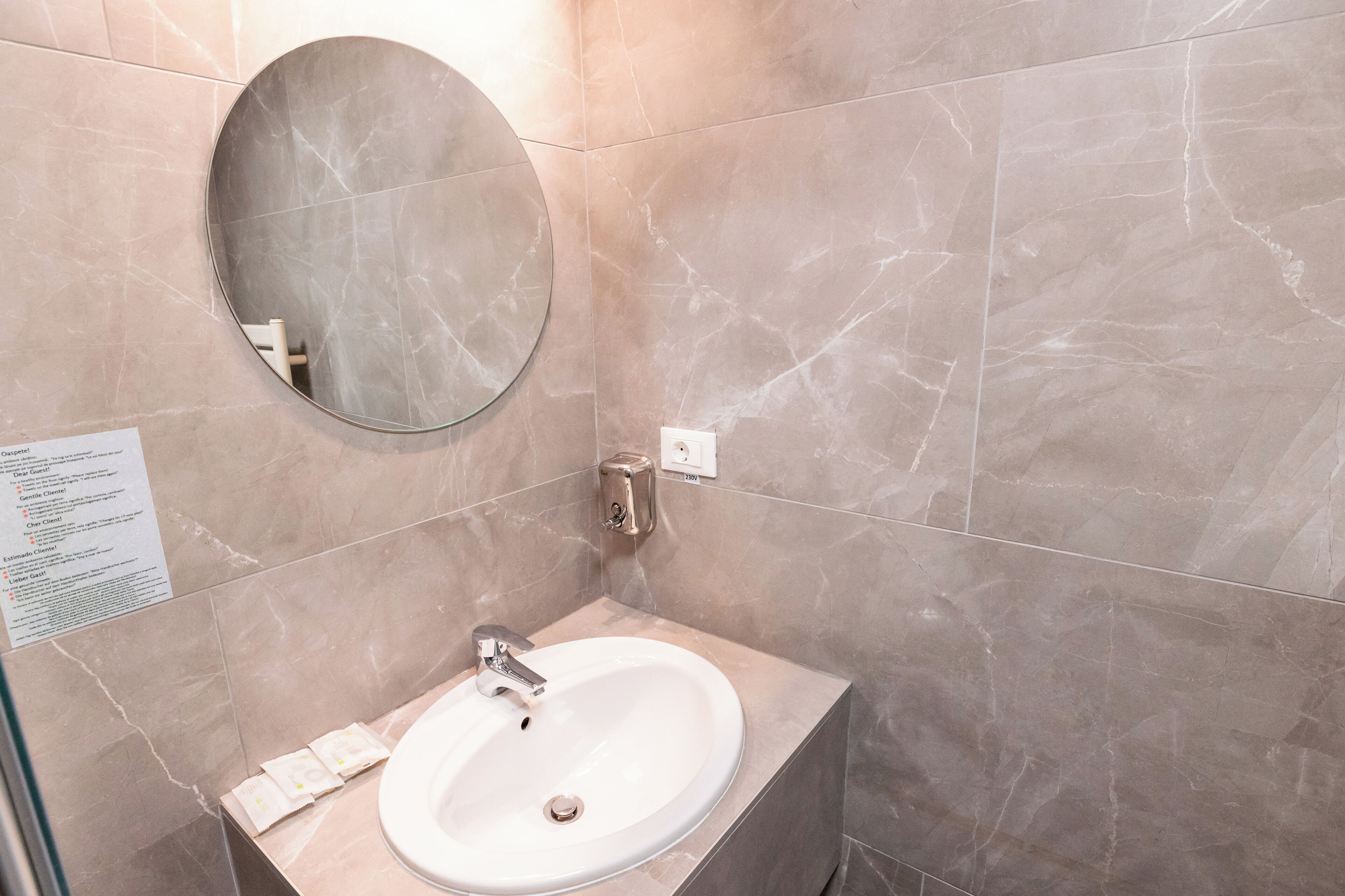 A bathroom with a round mirror, a sink, and a marble-tiled wall.