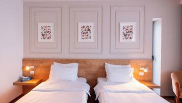 Habitación de hotel con dos camas, cabecero de madera, cuadro floral enmarcado en la pared, lámparas de noche y una silla.