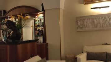 A cozy living room with a sofa, a small table, and a bar area with bottles and flowers.