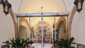 A hotel entrance with a glass door, arched stone walls, and potted plants. - Akropolis Hotel (Taranto)
