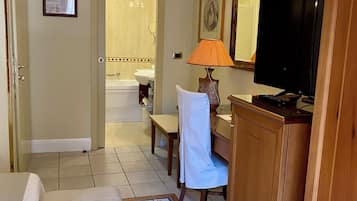 Habitación de hotel con sofá, escritorio con lámpara, televisión y baño visible a través de una puerta abierta.