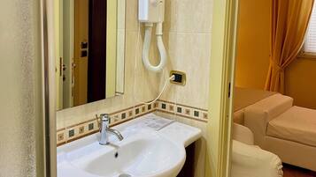 A bathroom with a sink, mirror, towel dispenser, and a glass shower enclosure.