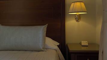 Una cama bien hecha con sábanas blancas, cabecera de madera, lámpara de noche y mesita con un teléfono.