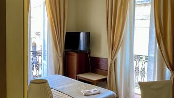 A hotel room with a bed, a television, a desk with a telephone, and a chair.