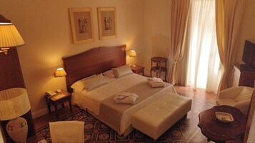 A hotel room with a large bed, two bedside lamps, a small table, a chair, and a television on a cabinet.