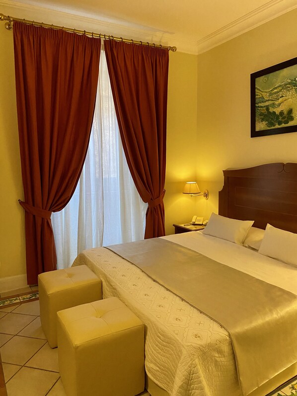 A hotel room with a large bed, two bedside tables, a nightstand, a lamp, and a painting on the wall.