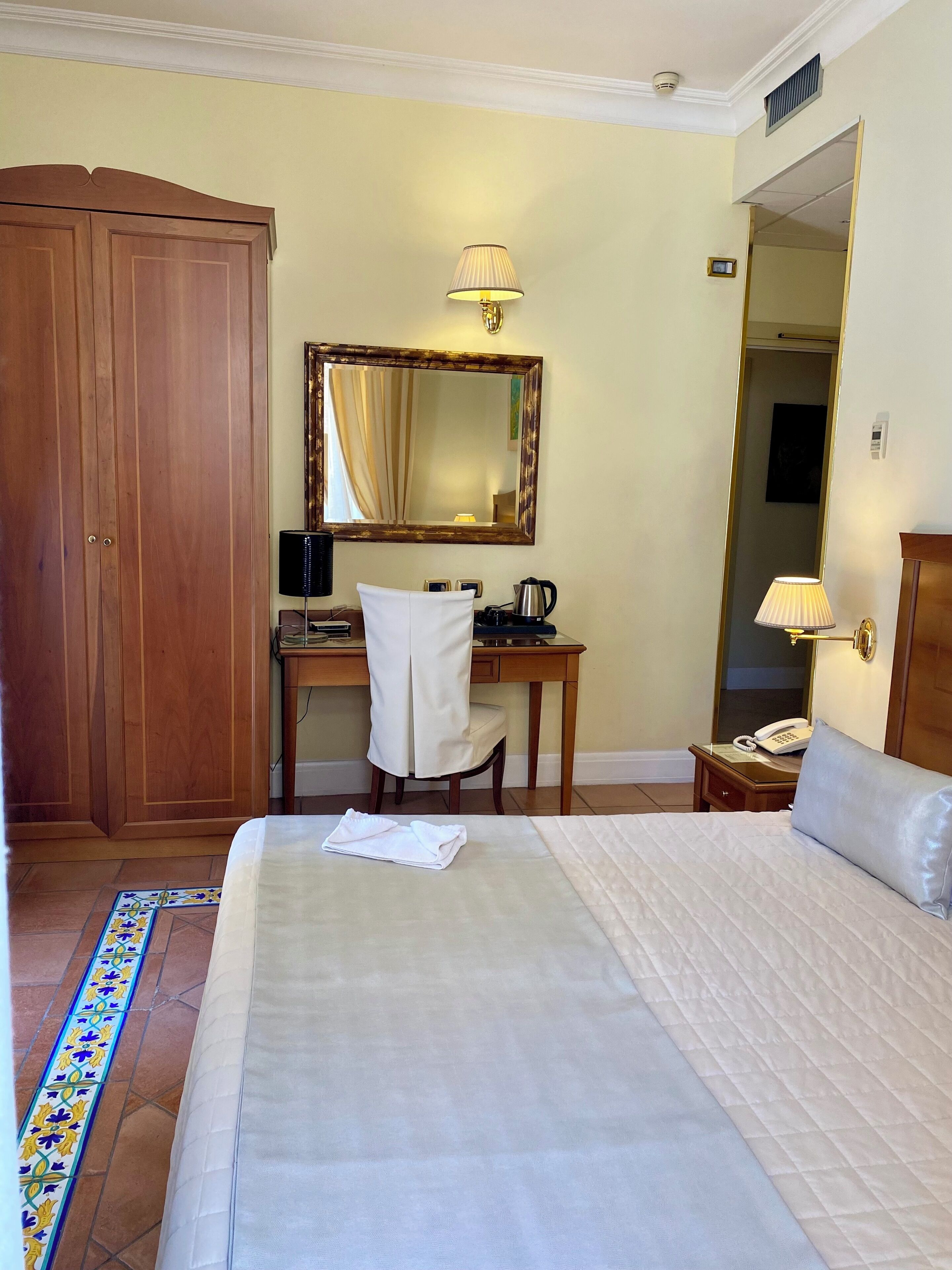 Una habitación de hotel con una cama, un escritorio con una silla, un teléfono, un espejo y un armario.