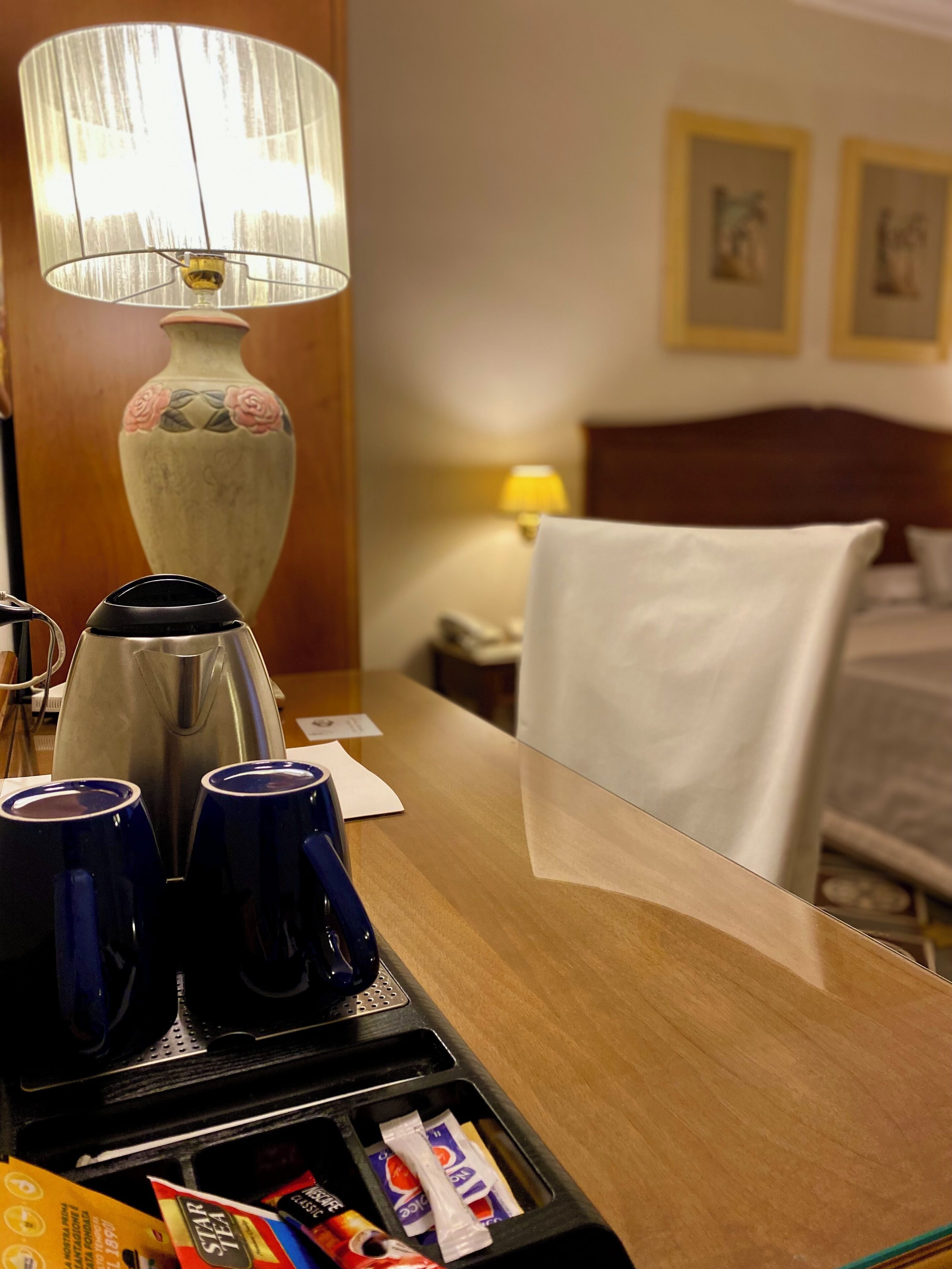 Una habitación de hotel con un escritorio de madera, una lámpara, un hervidor y una cama.