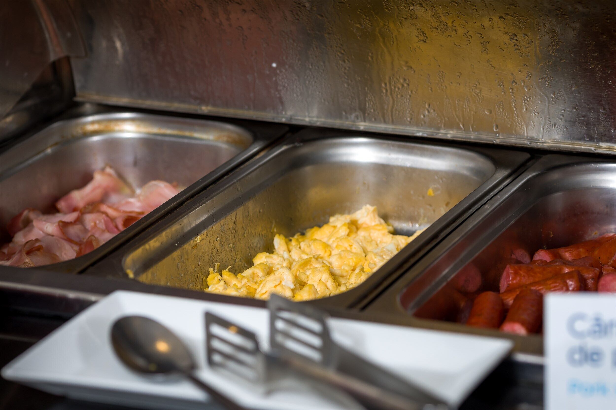 A buffet with various food options including scrambled eggs, bacon, and sausages.