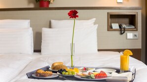 A neatly made bed with white linens, a tray with breakfast items including fruits, bread, and a glass of orange juice, and a red flower in a vase. - Hotel CH Bucharest (Bucharest)
