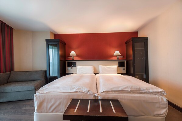 A hotel room with a double bed, two bedside tables, a sofa, a wardrobe, and a desk.