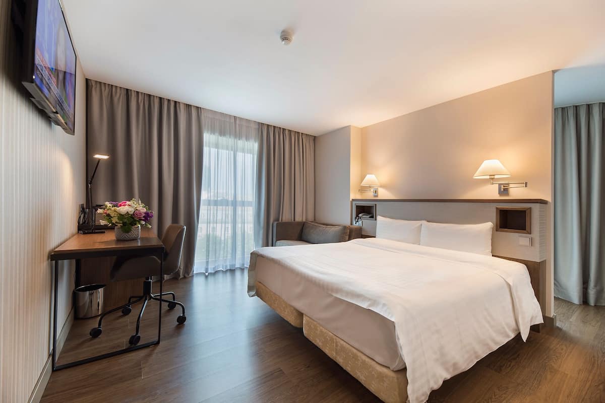Habitación de hotel con una cama grande, un escritorio con silla, un televisor montado en la pared y dos lámparas de noche.