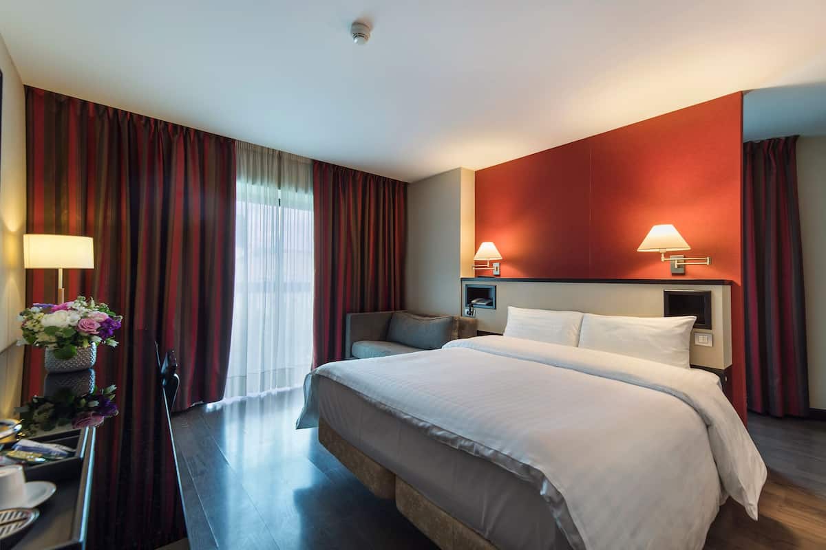 Habitación de hotel con una cama grande, dos lámparas de noche, un escritorio con lámpara y un jarrón con flores.