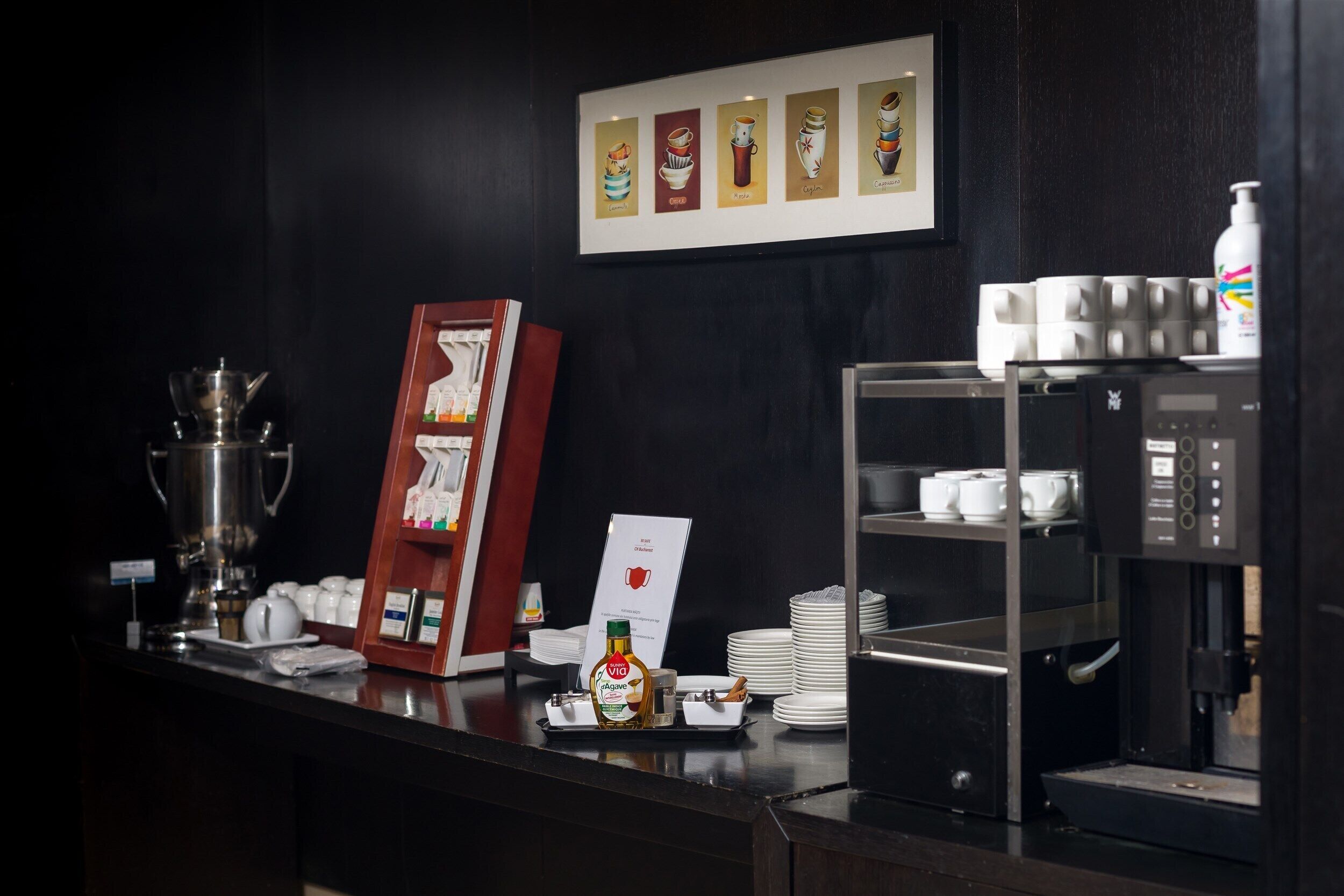 A hotel reception area with a coffee machine, a framed menu, and a display of coffee cups.