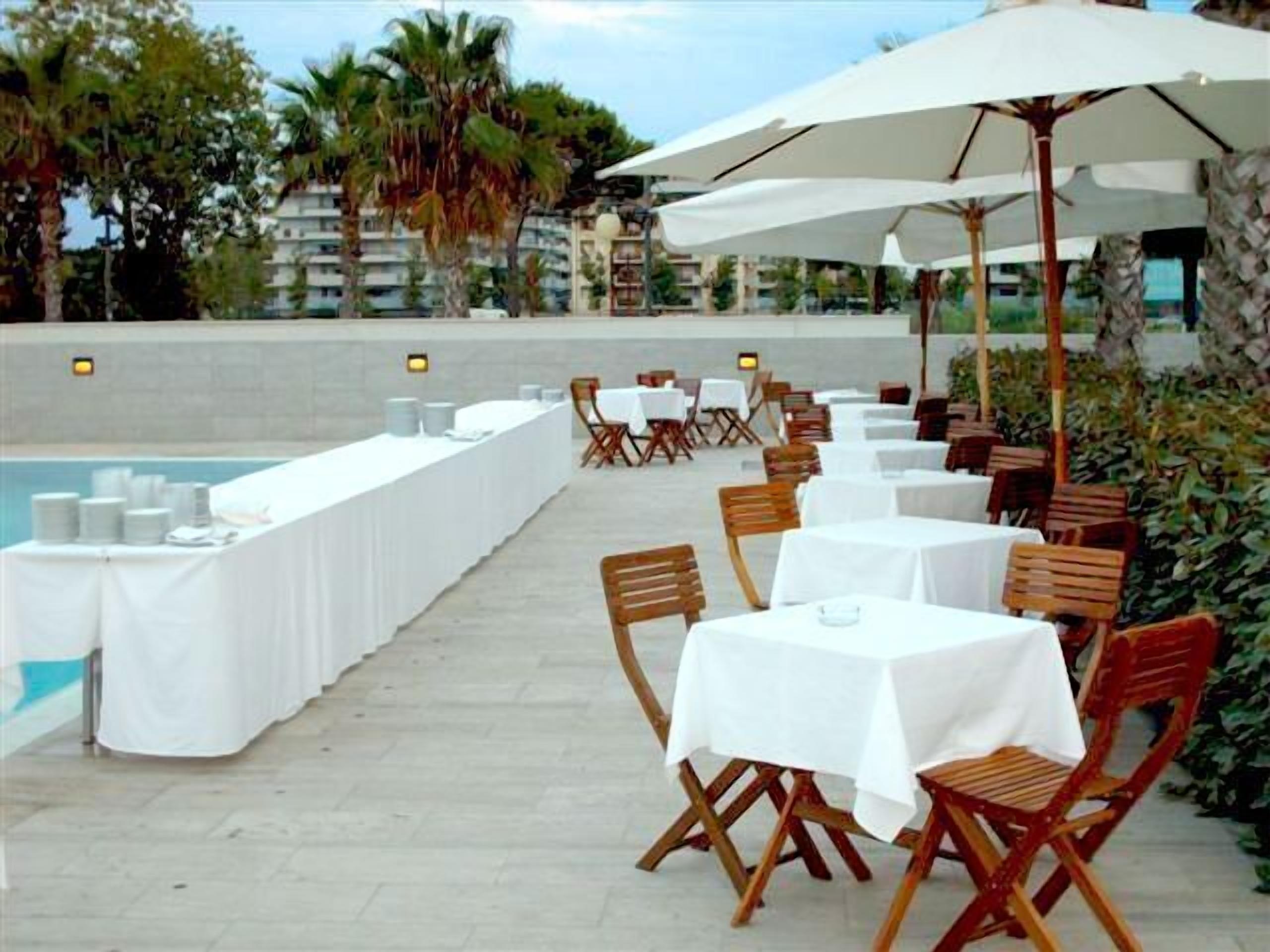An outdoor dining area with tables and chairs, a pool, and palm trees.