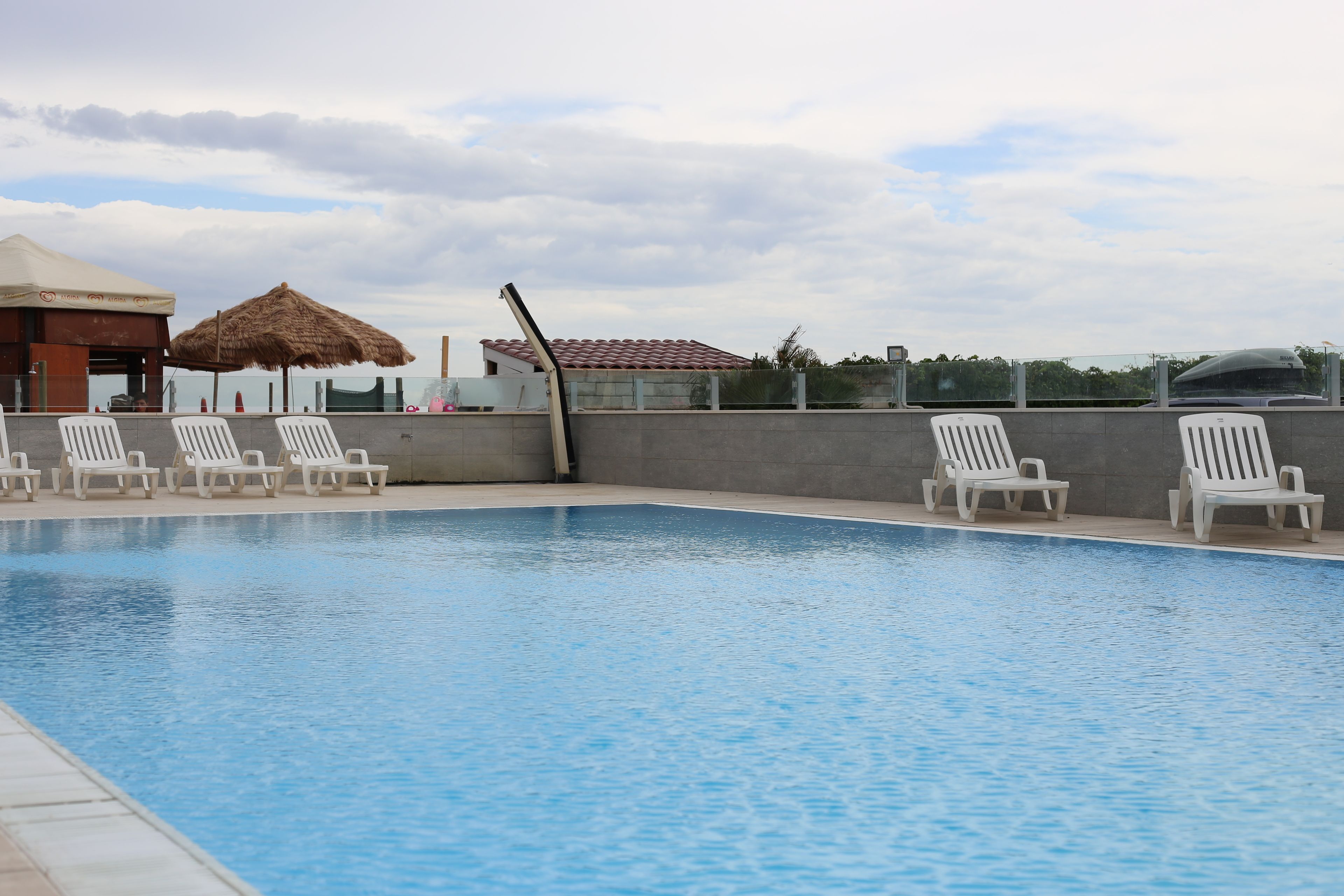 A swimming pool with lounge chairs, a thatched umbrella, and a view of the sky.