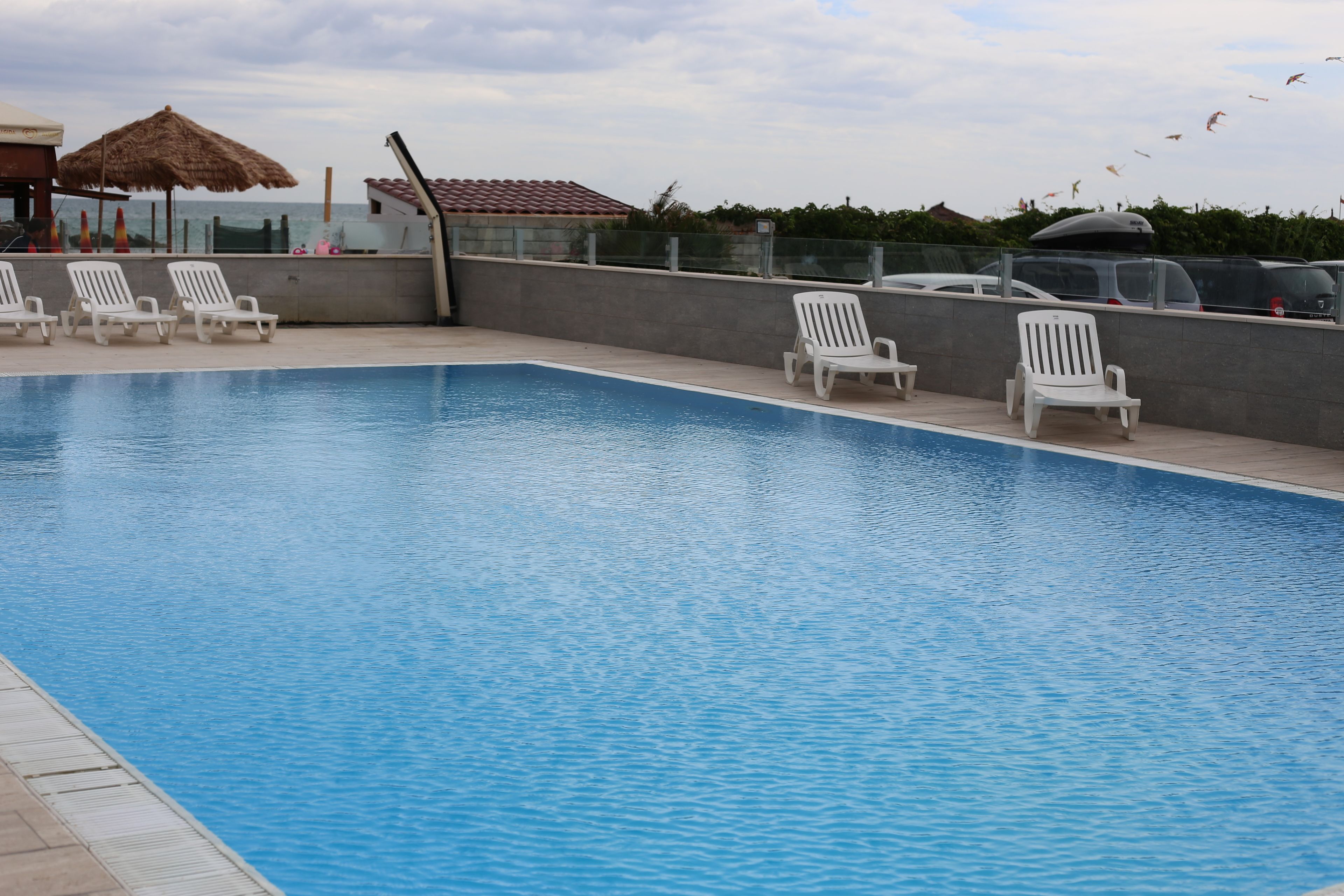 A swimming pool with white lounge chairs and a thatched umbrella.