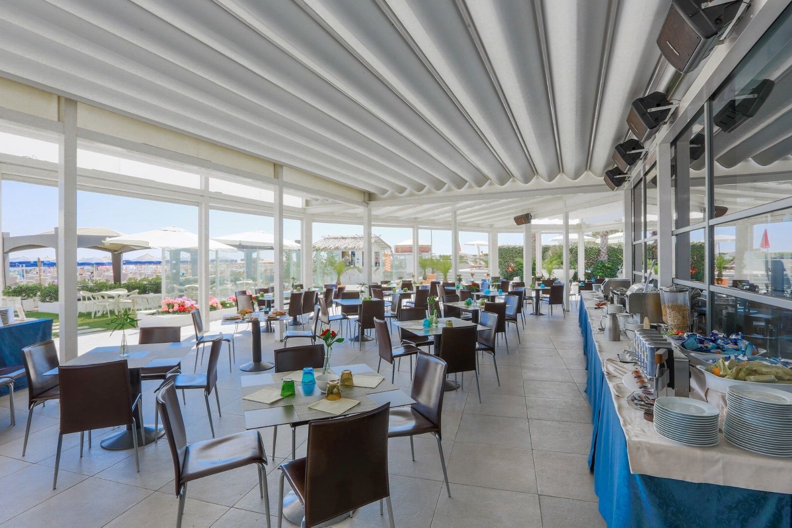 An indoor dining area with tables and chairs, large windows, and a buffet on the right.