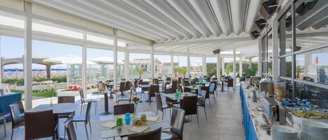 An indoor dining area with tables and chairs, large windows, and a buffet on the right.