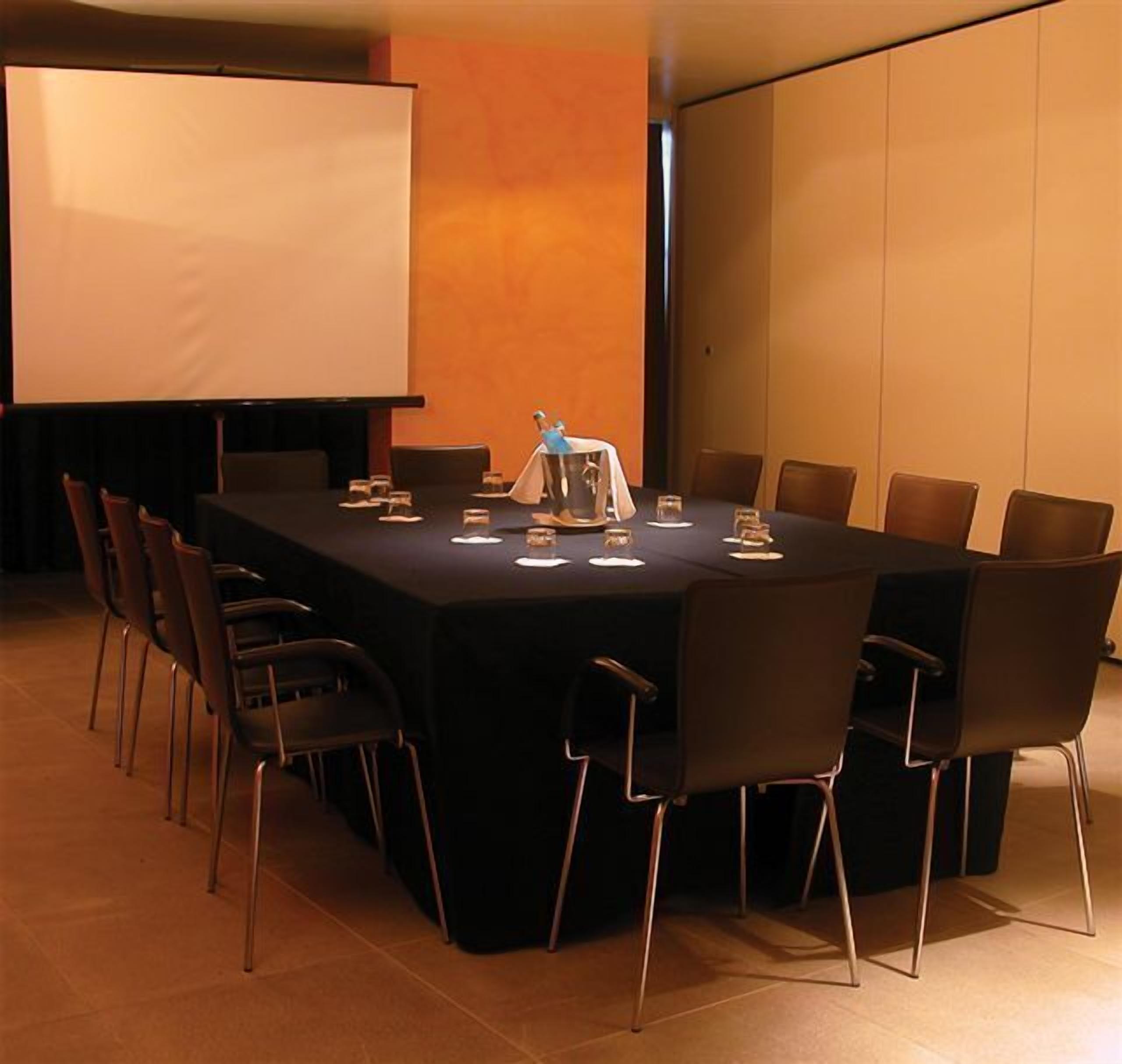 A conference room with a long table, chairs, a projector screen, and a whiteboard.