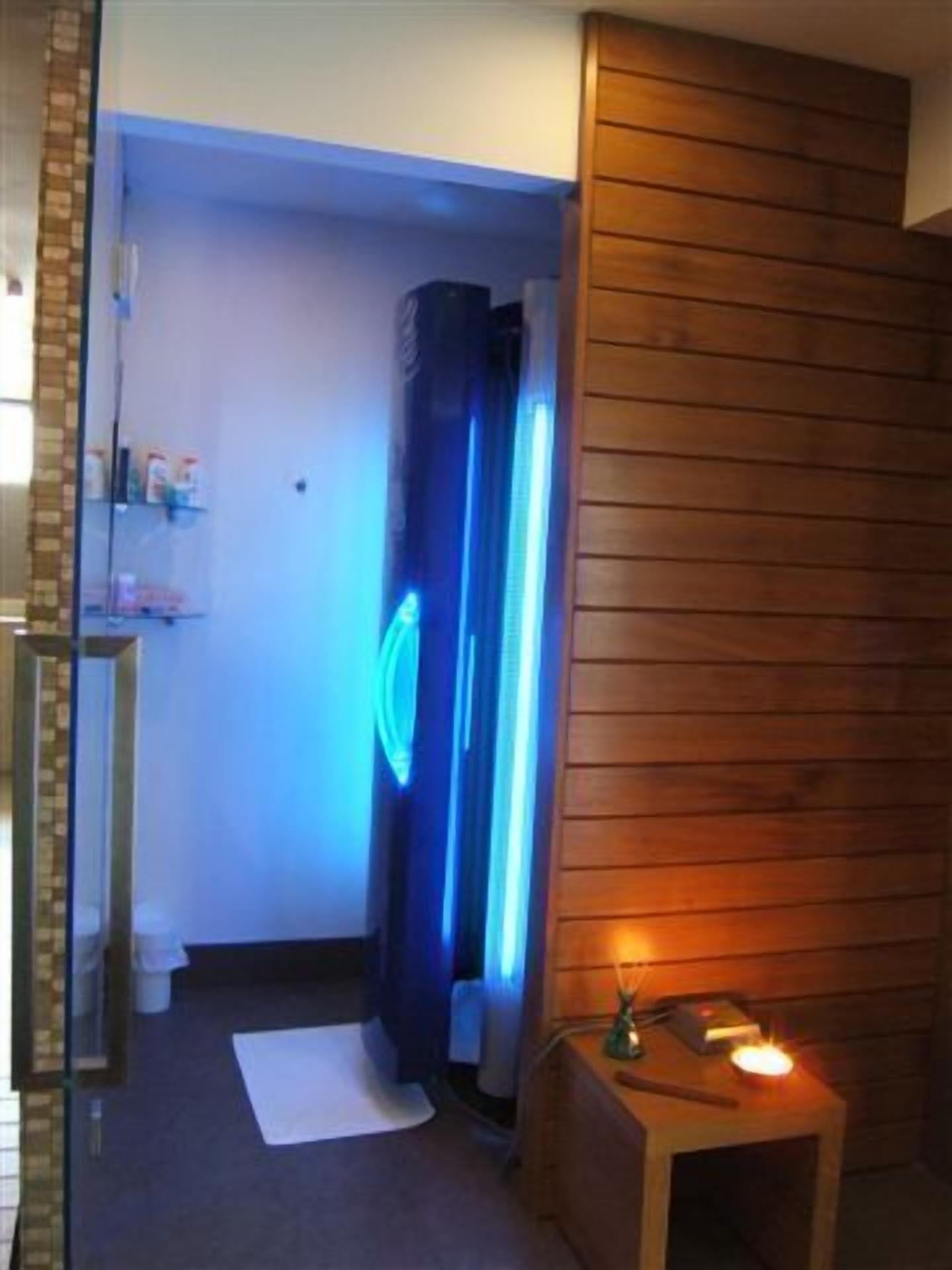 Una habitación con pared de madera, una pequeña mesa con vela y una lámpara azul.