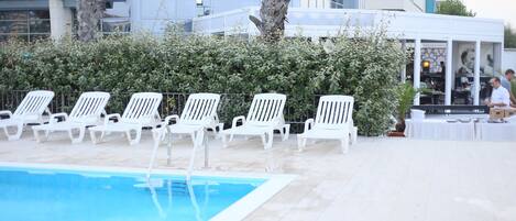 A poolside area with white lounge chairs and a pool.