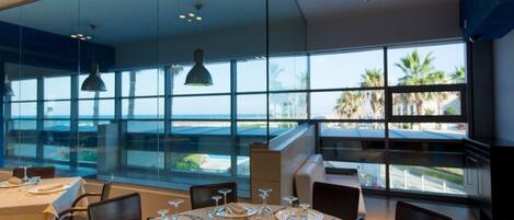 A restaurant with tables set for dining, large windows offering a view of the ocean, and a modern interior design.