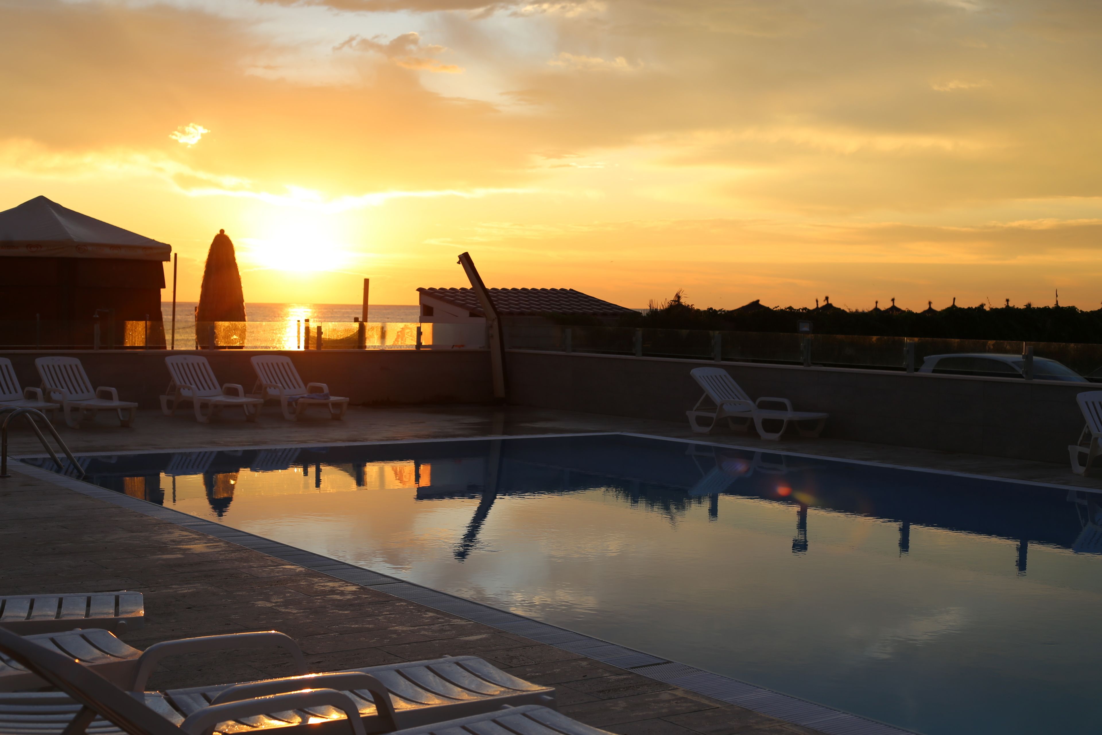 A swimming pool with lounge chairs and a view of the sunset over the ocean.