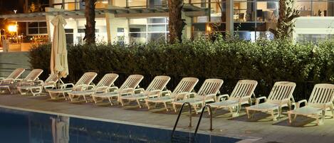 Un espace aménagé au bord de la piscine, avec des chaises longues et un palmier.