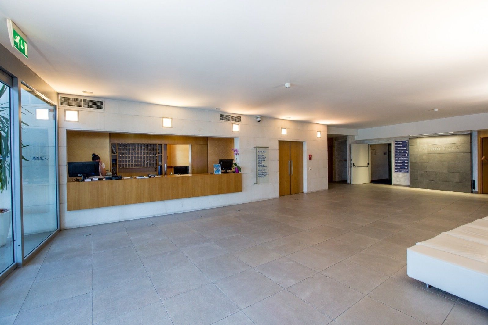 Zona de recepción de un hotel con un mostrador de madera, una computadora y un cartel que enumera los servicios del hotel.