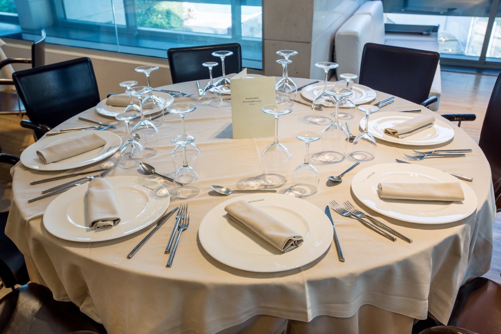 A round table set for a meal with plates, cutlery, and wine glasses.