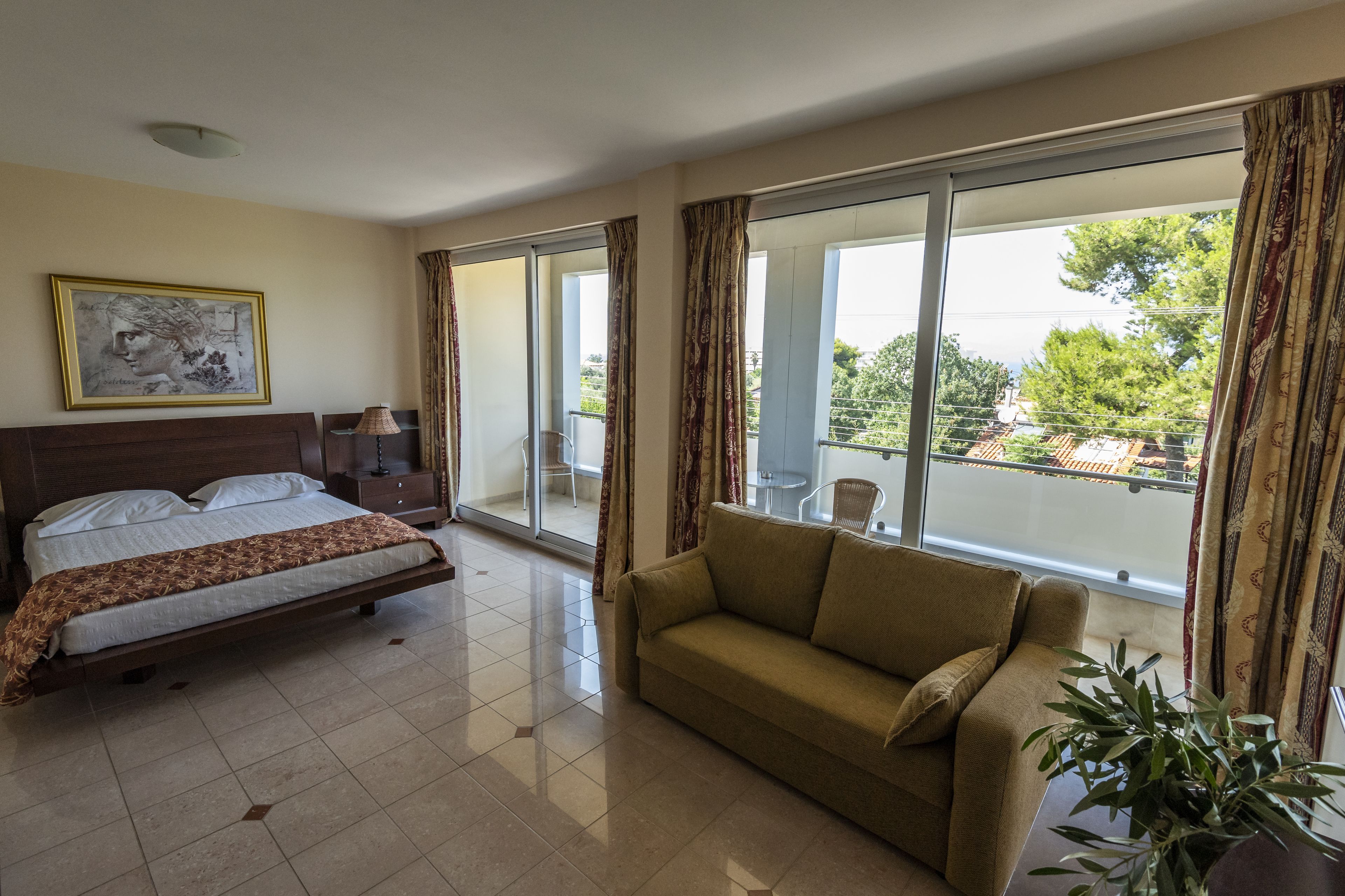 A hotel room with a bed, a sofa, a large window, and a painting on the wall.